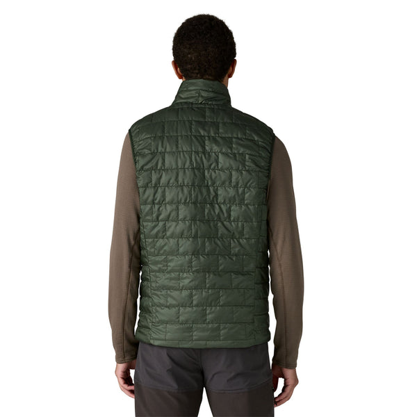 Person wearing the old growth green Patagonia Men's Nano Puff quilted vest and black pants on a white background.