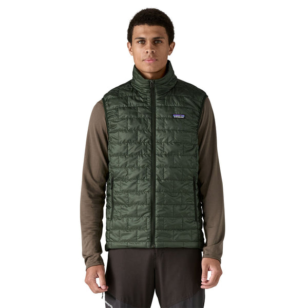 Person wearing the old growth green Patagonia Men's Nano Puff quilted vest and black pants on a white background.