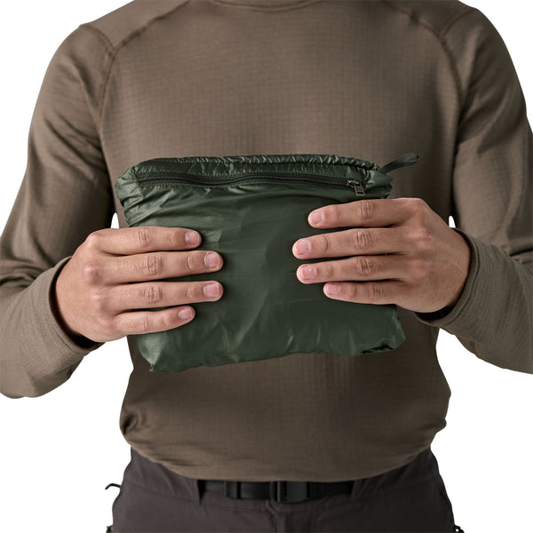 Person holding the old growth green Patagonia Men's Nano Puff quilted vest stuffed into it's own pocket, on a white background.