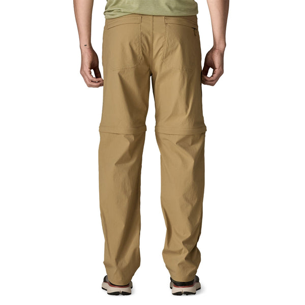 Person wearing the Classic Tan Patagonia Men's Quandary UPF Convertible Pants and a green shirt on a white background.