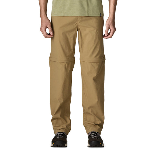 Person wearing the Classic Tan Patagonia Men's Quandary UPF Convertible Pants and a green shirt on a white background.