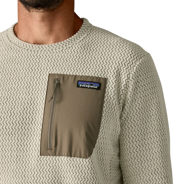 Close-up of front pocket on a beige Patagonia R1 Air Fleece textured shirt with a Patagonia logo on a white background.