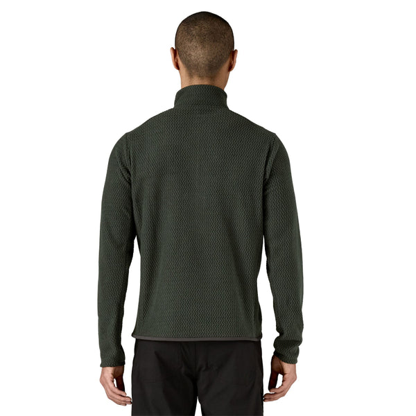 Person wearing an old growth green Patagonia Men's R1 Air Zip Neck Fleece Shirt with black pants on a white background.