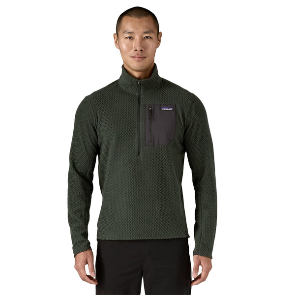 Person wearing an old growth green Patagonia Men's R1 Air Zip Neck Fleece Shirt with black pants on a white background.