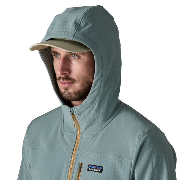 Man wearing grey pants and the blue sage hooded Patagonia Men's R2 Techface Pullover showing hood deatil on a white background.