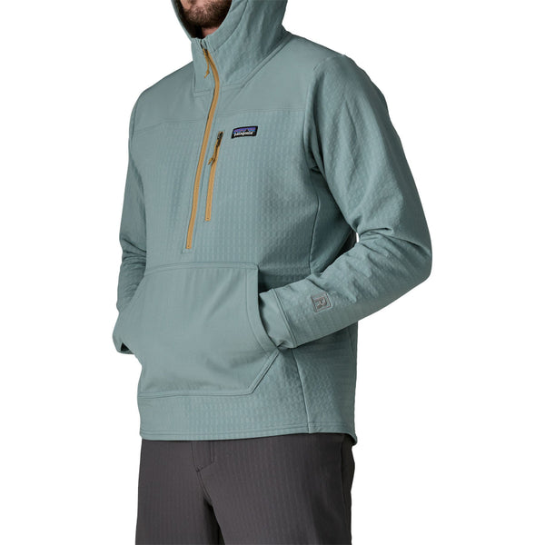 Man wearing grey pants and the blue sage hooded Patagonia Men's R2 Techface Pullover showing zipper front pocket detail on a white background.