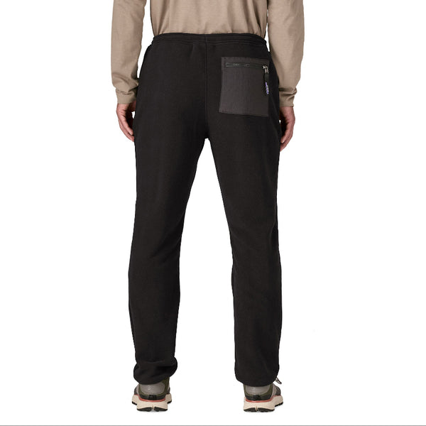 A person wearing a tan long sleeved shirt and lack solid color Patagonia Men's Synchilla Fleece Pants with an elastic waistband and zipper panelled back right pocket, against a white background.