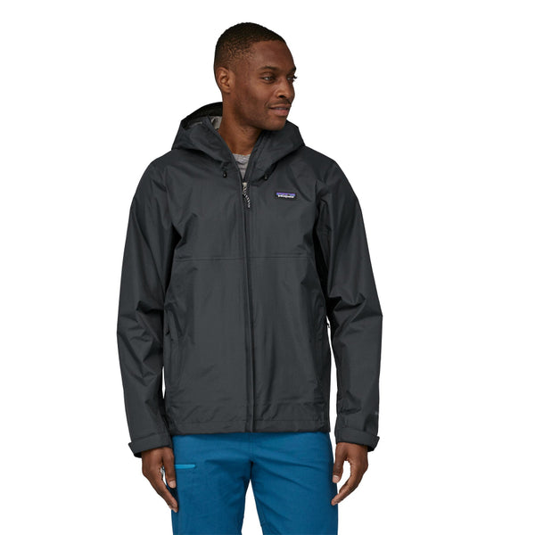 Person wearing a Patagonia Men's Torrentshell 3L Rain Jacket in black and blue pants on a white background.