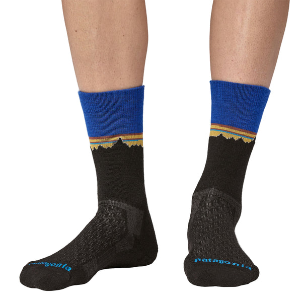 Person wearing Black Patagonia Merino Crew socks with blue top and yellow fitz roy stripe on a white background.