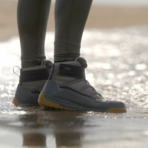 Person wearing noble grey Patagonia River Salt II Wading Boots, standing on the beach at the edge of the surf.