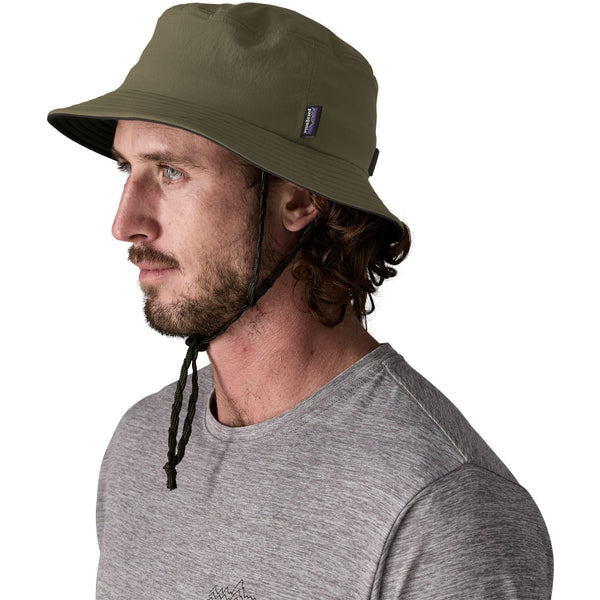 Person wearing a grey t-shirt and the basin green color Patagonia Surf Brimmer Bucket Hat, on a white background.