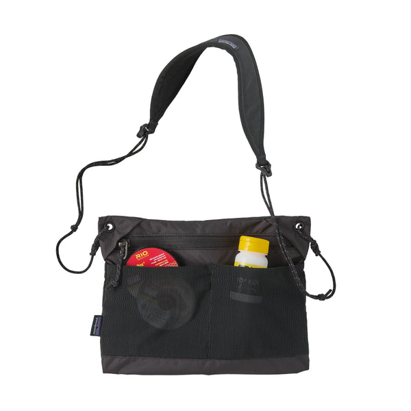 Black Patagonia Terravia Sacoche crossbody bag with accessories (not included) shown in the front pockets, on a white background.