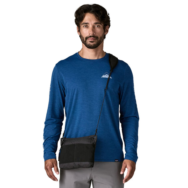 Man wearing a blue long-sleeve shirt with a black Patagonia Terravia Sacoche crossbody bag in front on a white background.