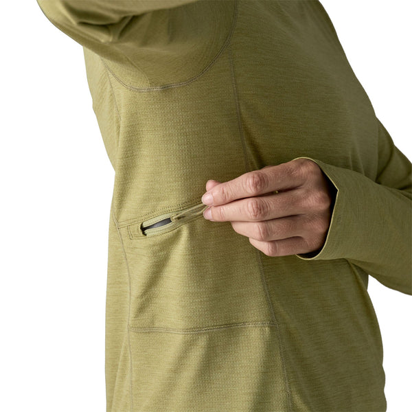 Person wearing a gumtree green x-dye Patagonia Women's Capilene Cool Sun Hoody showing the side zipper pocket details, against a white background.