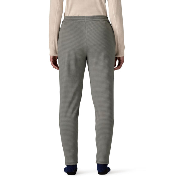 Person seen from the back wearing a light pink top and noble grey Patagonia Women's R1 Fleece Pants on a white background.