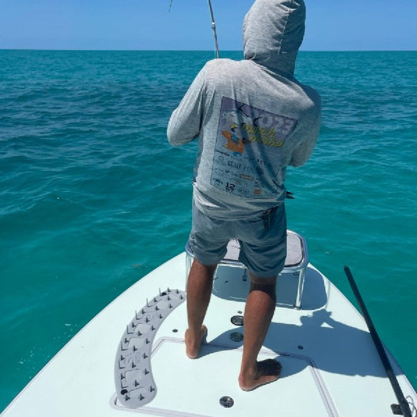 Person fly fishing on a flats skiff in tropical waters, using the SA Launch Pad Casting Mat to catch fly line coils.