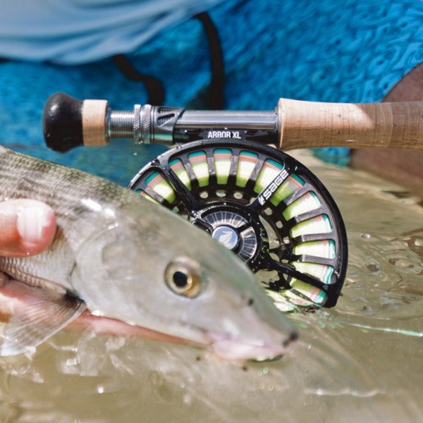 a single sage arbor xl fly fishing reel in the slate color seated on a fly rod and partially submerged in saltwater behind a hand holding a bonefish in the water