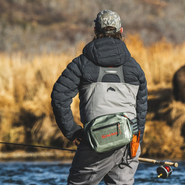 Person in waders with a spey rod  and wearing the Simms Dry Creek Z Waterproof Waist Pack, surveying the river and opposing bank.