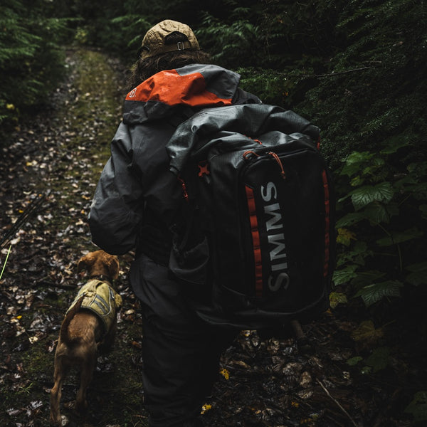 Person walking a dog on a trail with a Simms G3 Guide Rolltop Backpack.