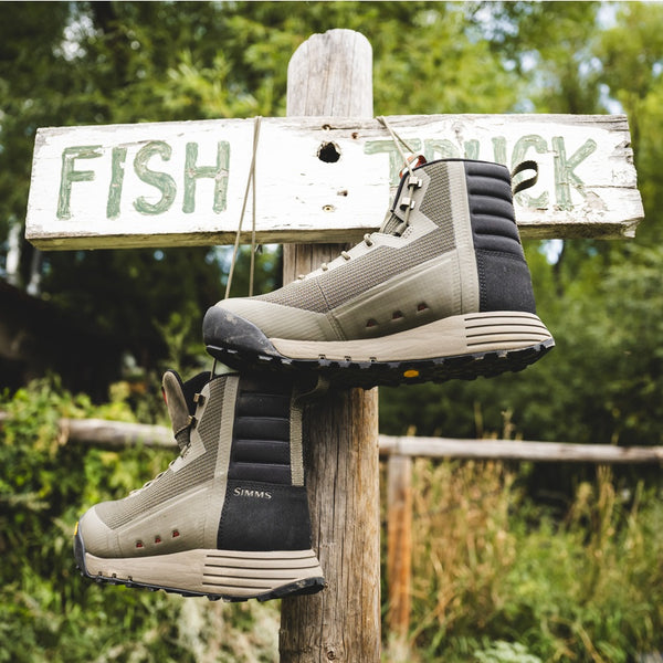 Pair of Simms Men's Access Wading Boots hanging on a wooden post with 'FISH TRUCK' sign in the background.