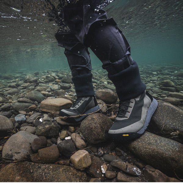Person wearing waders and the Simms Men's Access Wading Boot, standing on rocks underwater.
