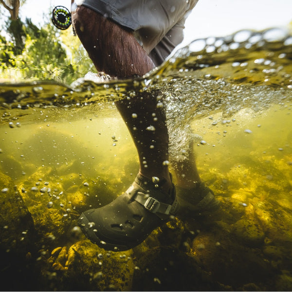 Underwater view of a person with a fly fishing rod and wearing khaki shorts and dark stone brown and beige Simms Men's Drifter AT Fishing Shoe.
