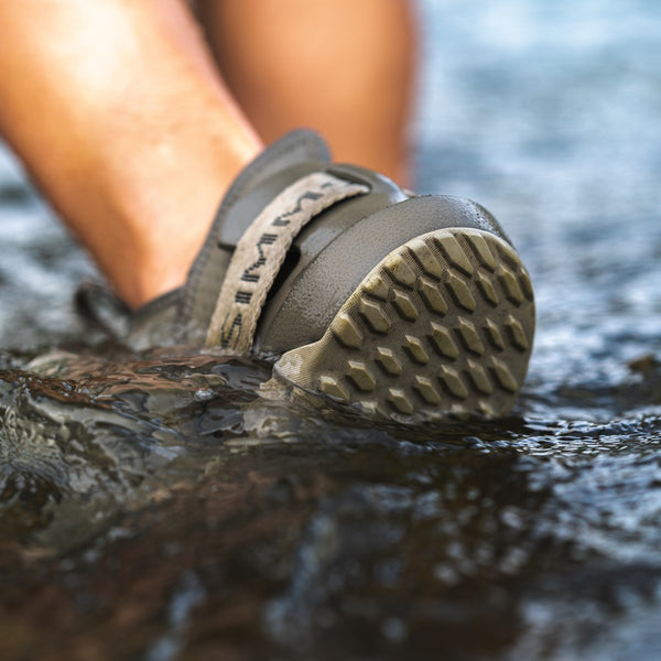 Close up view of a person wearing dark stone brown and beige Simms Men's Drifter AT Fishing Shoe walking through shallow water.