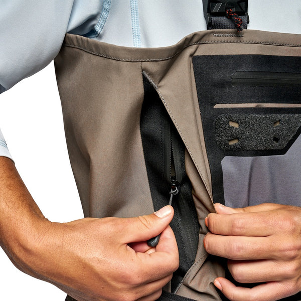 Close up of a person doing up the zipper on the passthrough front pocket on the Simms Men's G3 Pro GORE-TEX Stockingfoot Waders for fishing in dark elkhorn color.