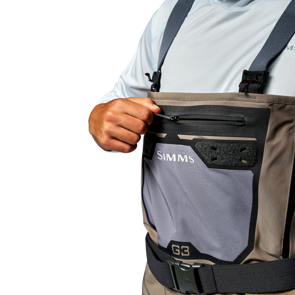 Close up of a person doing up the zipper on the front drop pocket on the Simms Men's G3 Pro GORE-TEX Stockingfoot Waders for fishing in dark elkhorn color.