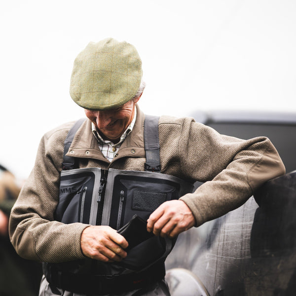 Man outdoors in Scotland wearing Simms G4Z Fly Fishing Waders over a Simms Harbor Fleece Sweater, folding a fly rod sock. 