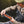 Man sitting next to a river in Scotland wearing Simms G4Z Fly Fishing Waders over a Simms Harbor Fleece Sweater, choosing a bright orange fly from an open fly box in his hands.