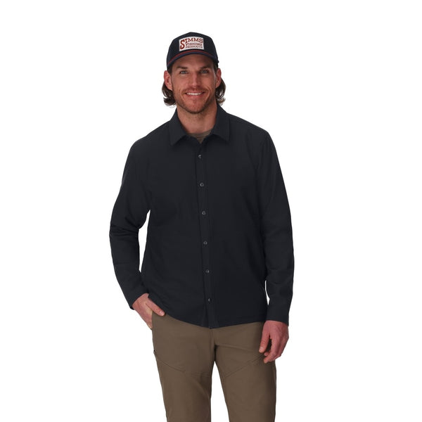 Front view of a person wearing a black Simms Men's Harbor Shacket and cap on a white background.