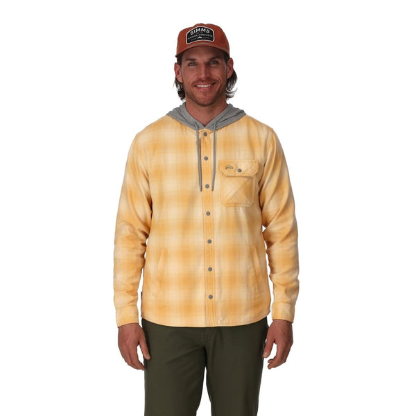 Front view of a man wearing a Simms Men's Santee Flannel Hoody in yellow plaid with a grey hood, green pants, and an orange ball cap on a white background.