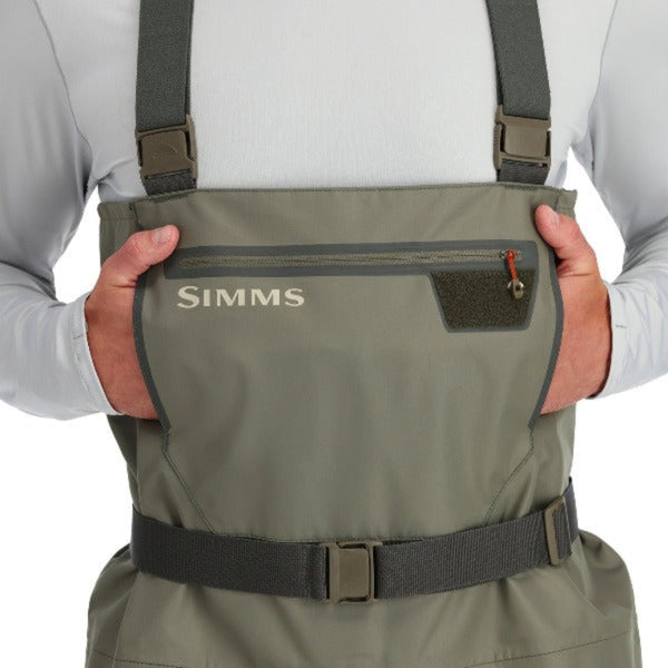 A person facing forward wearing Simms Men's Tributary Stockingfoot Waders zoomed in on the front pocket on a white background.