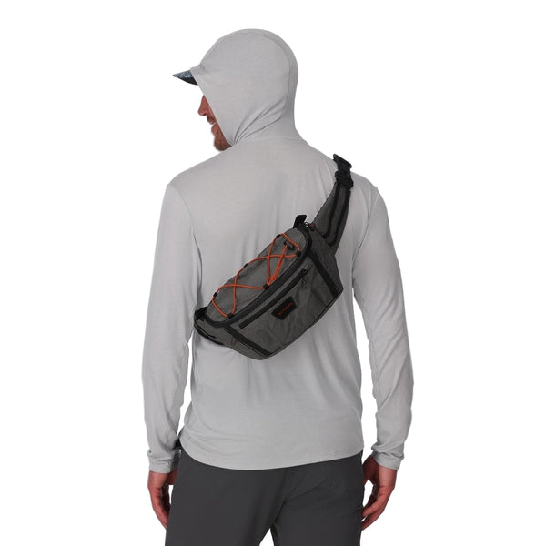 Person wearing a light gray hoodie with a Simms Scout Hip Pack as a sling pack on a white background.
