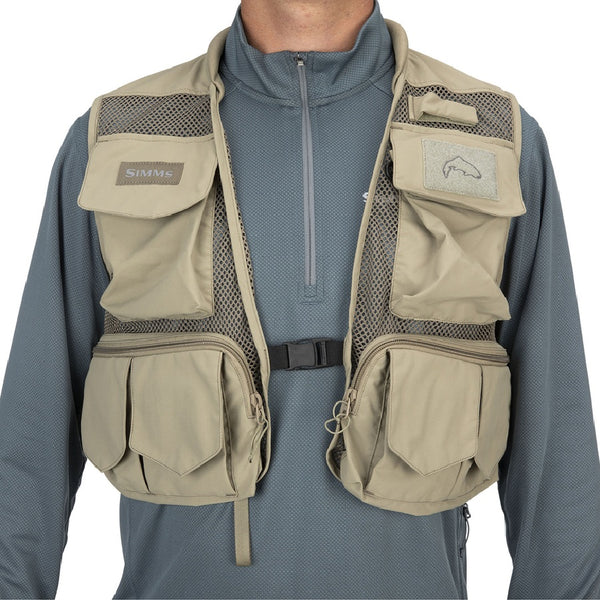 Front view of a person wearing the tan Simms Tributary Fishing Vest showing multiple pockets and mesh design on a white background.