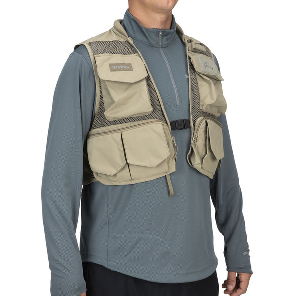 Side view of a person wearing the tan Simms Tributary Fishing Vest showing multiple pockets and mesh design on a white background.