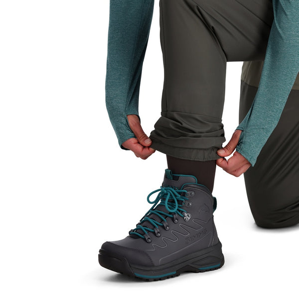 A person kneeling forward wearing Simms Women's Tributary Stockingfoot Waders zoomed in on the leg and gravel guard details on a white background.