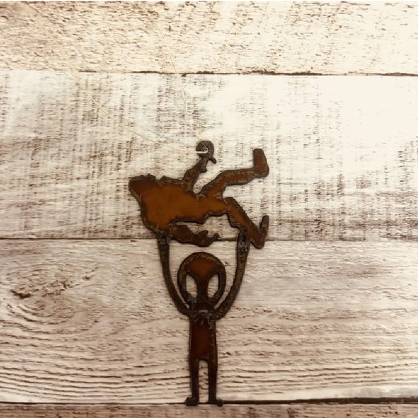 Metallic brown Universal Ironworks Alien Holding Bigfoot Ornament, on a light wooden background.