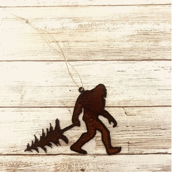 Metallic brown Universal Ironworks Sasquatch with Tree Ornament, on a light wooden background.
