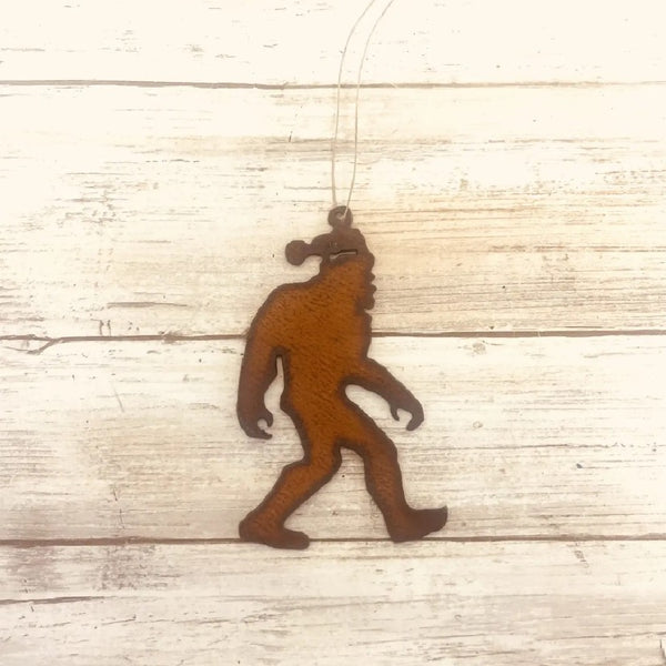 Metallic brown Universal Ironworks Sasquatch with Santa Hat Ornament, on a light wooden background.
