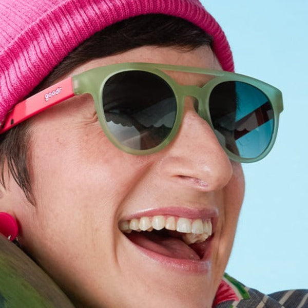 Person wearing Watermelon Wasted Goodr PHG Sunglasses with green lenses and green and red frames on a light blue background.
