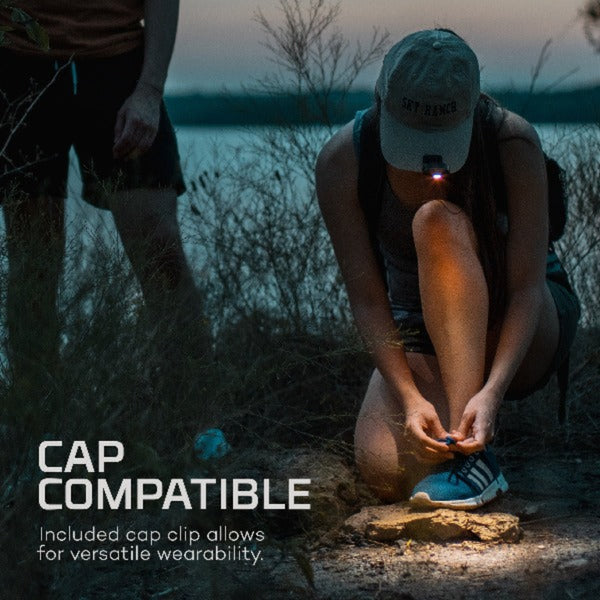 Person tying shoelaces with a Nebo Mycro headlamp on a ballcap's brim, near water at dusk.