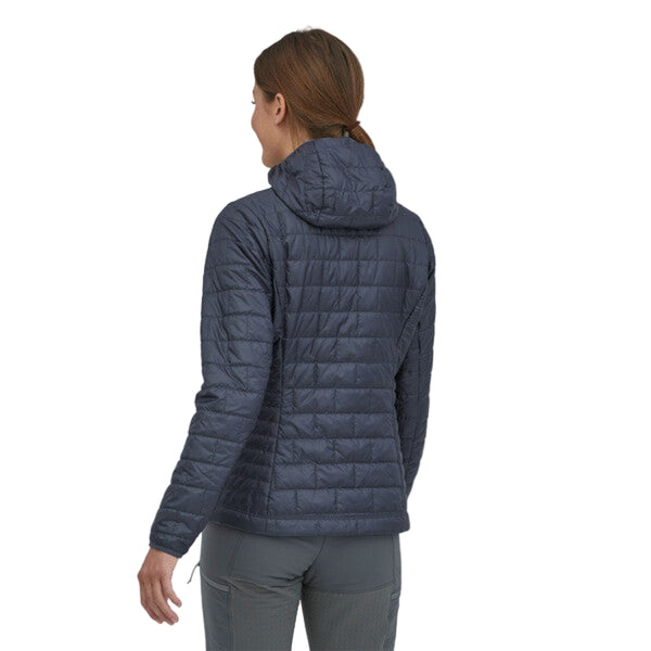 Person wearing the smolder blue Patagonia Women's Fitz Roy Trout Nano Puff Hoody and grey pants on a white background.