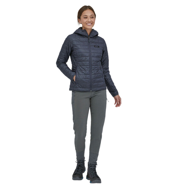 Person wearing the smolder blue Patagonia Women's Fitz Roy Trout Nano Puff Hoody and grey pants on a white background.