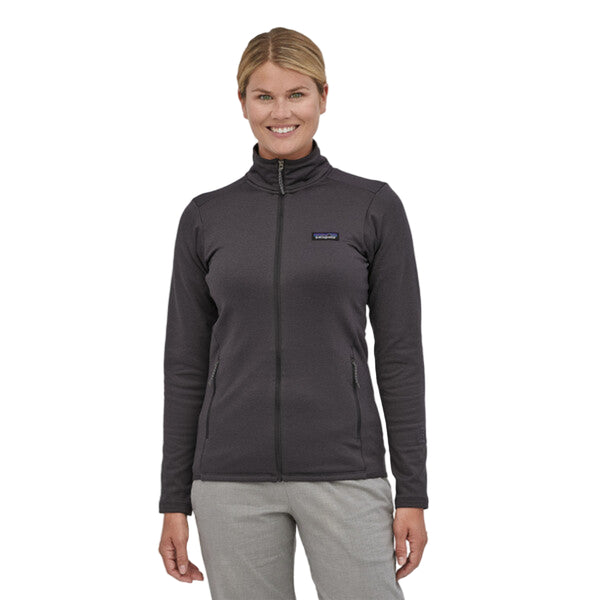 Person wearing a Patagonia Women's R1 Daily Jacket in black color with a zippered front, off-shoulder seams, and two zippered front pockets, on a white background.